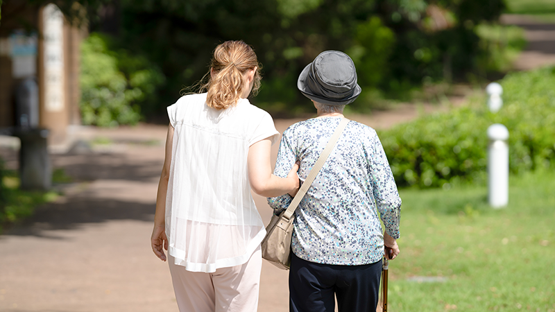 高齢者を支えながら歩く女性