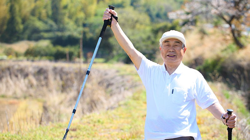 ノルディックポールを持って元気よくウォーキングする高齢者