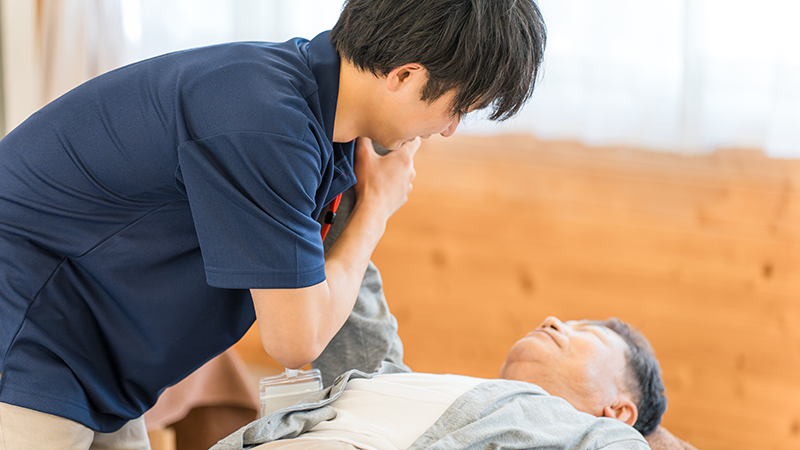 脳卒中の後遺症のため起き上がり介助を受ける高齢者男性